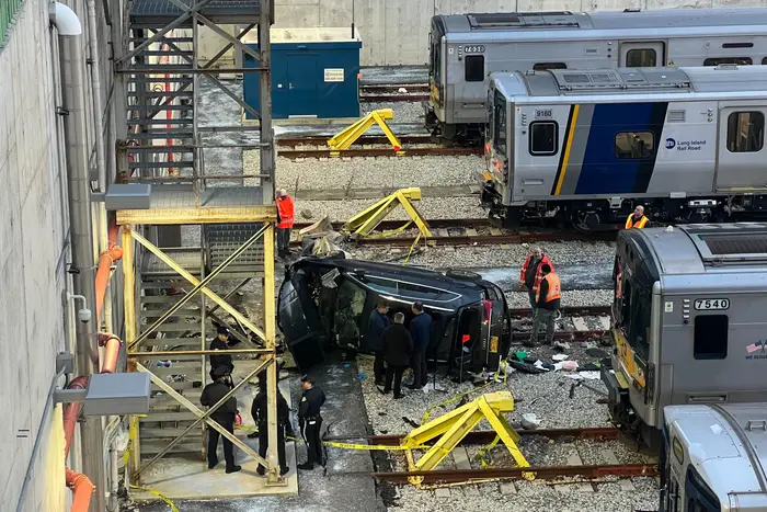 First responders surround a black Audi SUV, which is on its side in a trainyard.